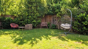 Un jardin avec une pelouse verdoyante, une clôture en bois et trois chaises en osier.