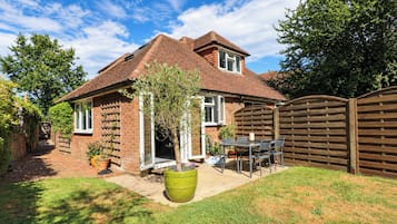 A house with a brick exterior, a tiled roof, a front door, and a fenced backyard with a patio table and chairs.