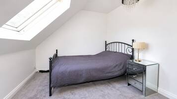 Une chambre avec un lit simple, une table de chevet avec des tiroirs, une lampe et une lucarne.
