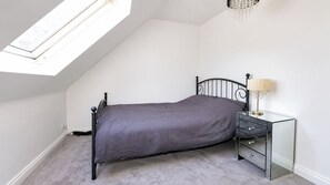 Une chambre avec un lit simple, une table de chevet avec des tiroirs, une lampe et une lucarne.