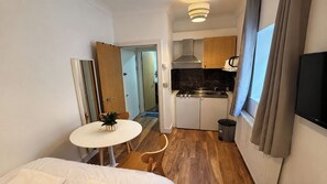 A compact hotel room with a kitchenette, a dining area with a table and chairs, a bed, and a television mounted on the wall. - Acton 1-Bed Apt, Sleeps 2 near Rosemont Rd Station (London)