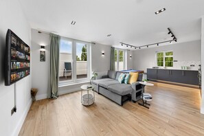 Un salon moderne avec un canapé gris, une petite table ronde et un téléviseur fixé au mur.