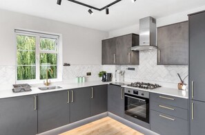 A modern kitchen with grey cabinets, a stainless steel range hood, and a window with a view of greenery. - 2bedroom 2bathroom Penthouse Wembley stadium (Wembley)
