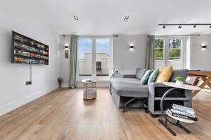A modern living room with a grey sofa, a small round table, and a bookshelf with various items. - 2bedroom 2bathroom Penthouse Wembley stadium (Wembley)