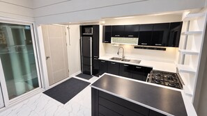 A modern kitchen with black cabinets, a stainless steel sink, and a gas stove. - Lovely apartment with large kitchen and fantastic terrasse perfectly located (Amphur Muang Satun)
