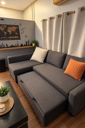 Ein modernes Wohnzimmer mit einer Eckcouch, einem kleinen Beistelltisch mit Pflanze und einer Weltkarte als Wandbild.