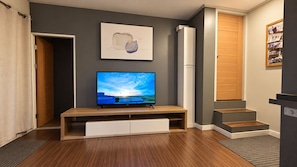 Ein Wohnzimmer mit einem Flachbildfernseher auf einem Holzboden, einem gerahmten abstrakten Gemälde an der Wand und einer Treppe, die in einen anderen Raum führt.