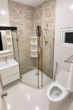 Un baño moderno con ducha envuelta en vidrio, inodoro y lavamanos con espejo.