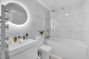 A modern bathroom with a glass shower enclosure, a round mirror, and a white sink with a potted plant. - Apartment Sleeps 7 with Wifi (London)