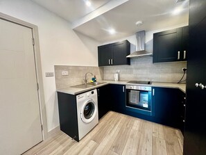 A compact kitchen with a built-in washing machine, a stove, and a sink. - Apartment Sleeps 5 near HIgh Street (Croydon)