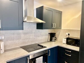A modern kitchen with grey cabinets, a built-in stove, a coffee maker, and a microwave. - Apartment Sleeps 5 near HIgh Street (Croydon)
