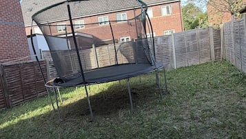 Een trampoline in een achtertuin, met een stenen huis op de achtergrond.