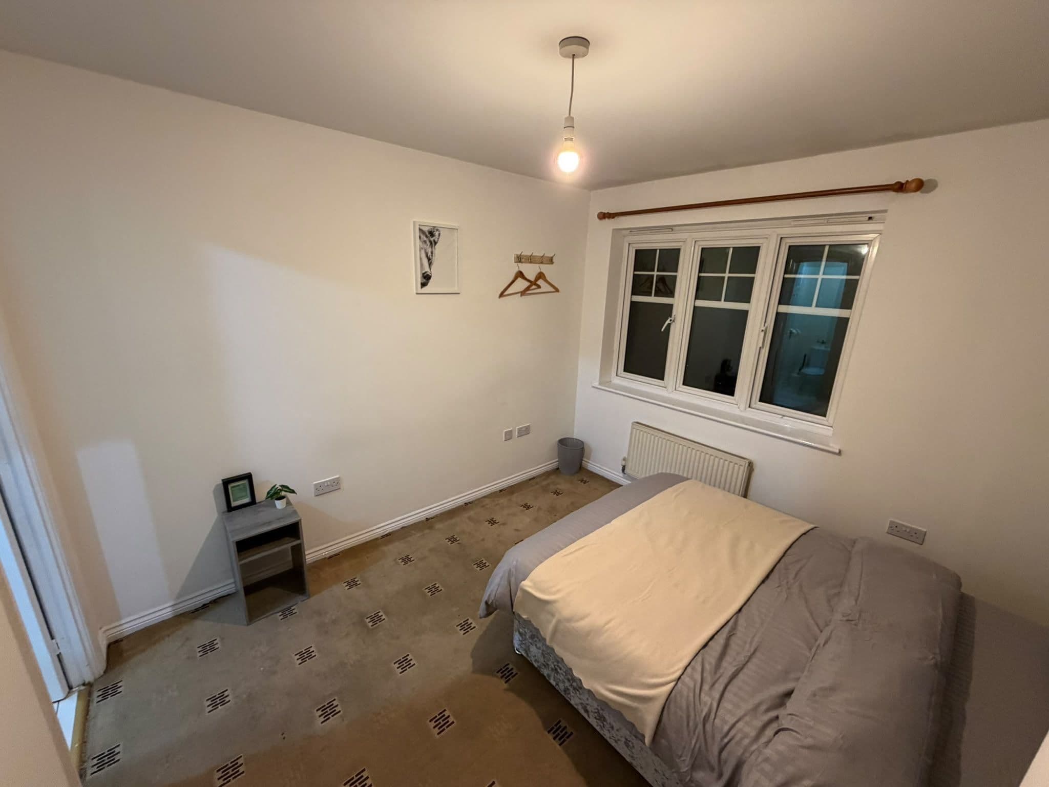 Een slaapkamer met een bed, een radiator, een raam en een wandlamp.