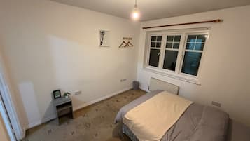 Een slaapkamer met een bed, een radiator, een raam en een wandlamp.