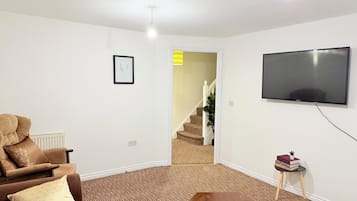 Una sala de estar con sofá, mesa de centro, televisor de pantalla plana y una escalera que conduce a otra habitación.