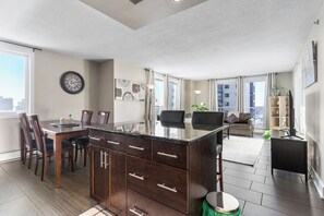 A modern kitchen with dark wood cabinets, a central island, and a dining area with chairs. - Downtown, 20th floor, river view, gym, free parking (Saskatoon)