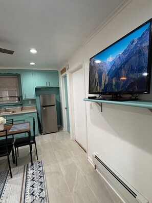 Eine moderne Küche mit türkis-farbenen Schränken, einem Edelstahl-Kühlschrank, einem Essbereich mit Tisch und Stühlen sowie einem Wand-Fernseher, der eine Berglandschaft zeigt.