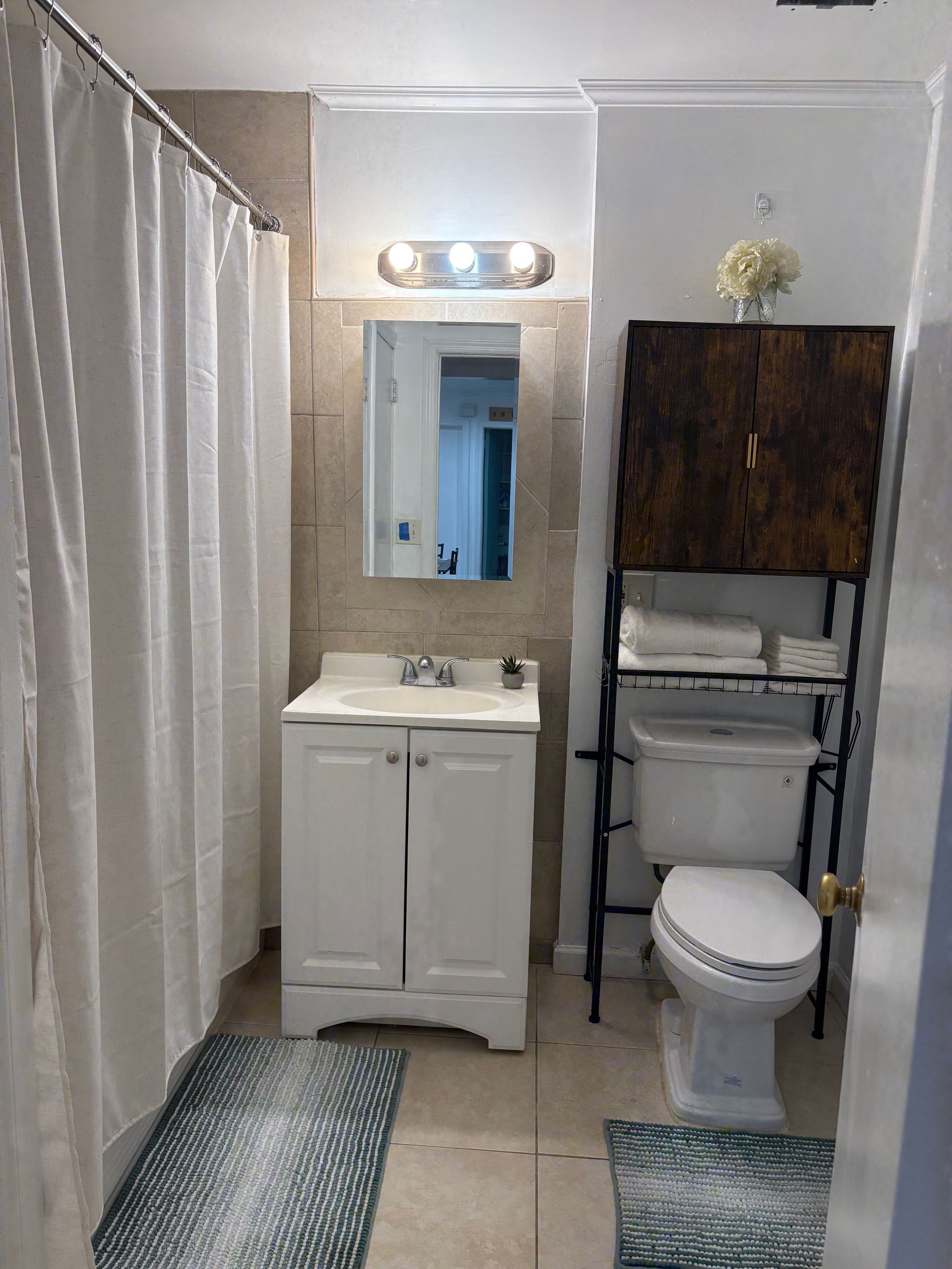 A bathroom with a shower curtain, a sink with a mirror above it, a toilet, and a cabinet with towels.