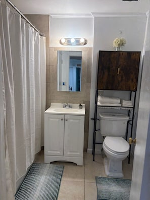 Ein Badezimmer mit Duschvorhang, Waschbecken mit Spiegel darüber, Toilette und einem Schrank mit Handtüchern.