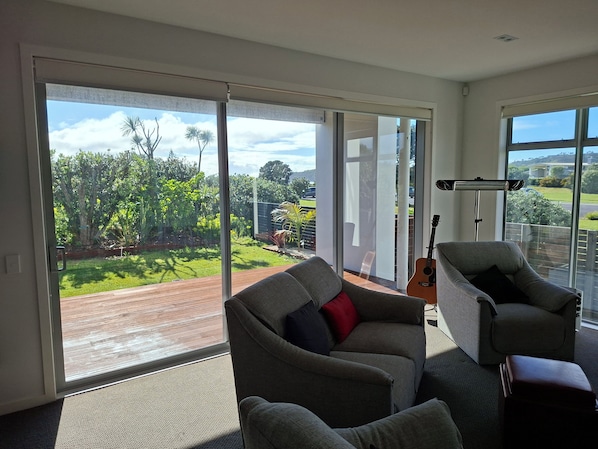 Ein Zimmer mit einer großen Glasschiebetür, die auf einen Balkon führt, einer Gitarre und zwei grauen Sesseln.