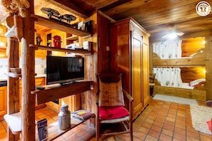 Ein gemütliches Blockhaus-Interieur mit Fernseher, Holzböden, einem Sessel und einem Bett mit Vorhängen.