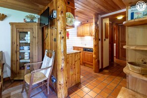 Ein rustikales Holzinterieur mit Essbereich, einer Küche mit Holzschränken und einem Stuhl mit gewebtem Sitz.