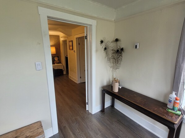 A hallway with a wooden floor, a white door, and a small table with a vase and a bottle.