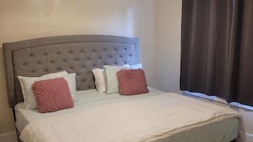 Una cama individual con cabecera capitonada, edredón blanco y ropa de cama estampada.