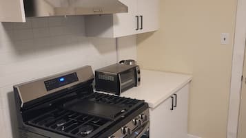Una cocina con estufa de acero inoxidable, un tostador y gabinetes blancos.