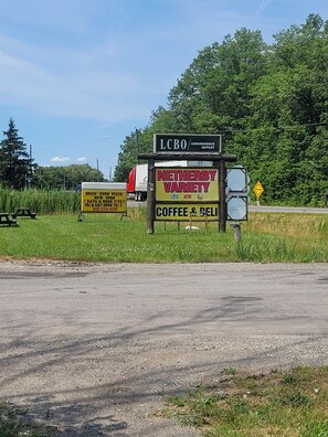 A roadside sign with multiple business advertisements including a convenience outlet, a pizza place, and a coffee & deli.
