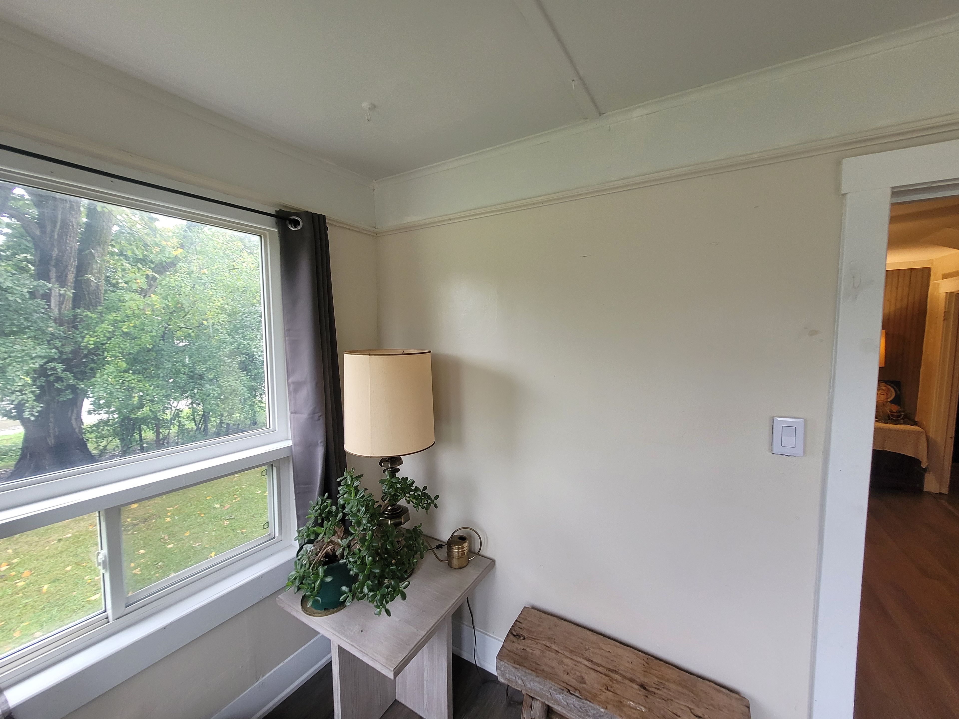 Una habitación con ventana, una lámpara, una mesita pequeña y un banco.