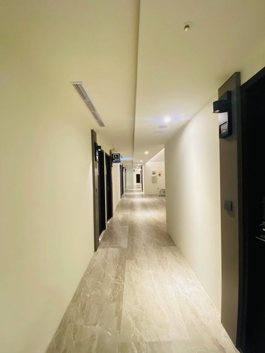 A hotel hallway with a marble floor, doors on both sides, and a sign indicating room number 1112.