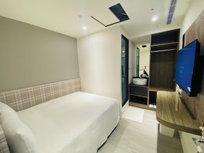 Una habitación de hotel con cama, baño con lavamanos y espejo, y televisor montado en la pared.