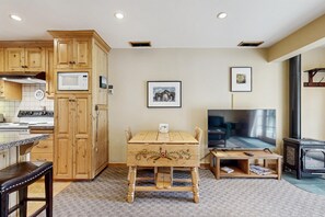 A compact kitchen with wooden cabinets, a microwave, a stove, and a dining area with a table and chairs. - 2BR Ketchum condo with fast WiFi, patio, and easy mountain access. (Ketchum)