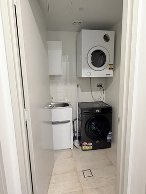 A laundry room with a washing machine, a dryer, and a small sink. - Panoramic Ocean 2BR, Gold Coast Spa & Pool (Southport)