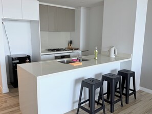 A modern kitchen with a central island, bar stools, a gas stove, and a built-in oven. - Panoramic Ocean 2BR, Gold Coast Spa & Pool (Southport)
