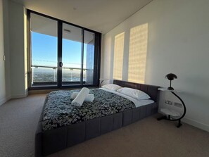 Una camera da letto con un letto grande, vista sulla città tramite finestre a tutta altezza e una lampada moderna.