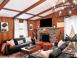 A cozy living room with a stone fireplace, wooden beams, a flat-screen TV, and a comfortable seating area. - The Hive at Big Bass Lake (Big Bass Lake)