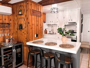 A modern kitchen with a central island, bar stools, and a welcoming sign. - The Hive at Big Bass Lake (Big Bass Lake)