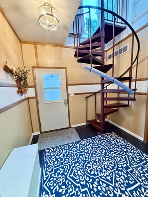 A spiral staircase with a wooden finish, a door with a window, and a patterned rug. - Kari’s Lakeshore Loft - Minutes from Houghton (Chassell)