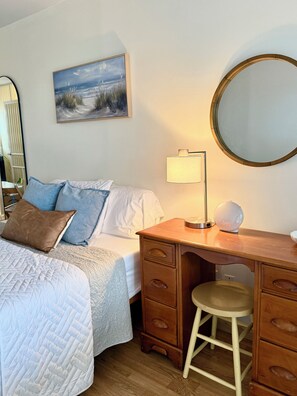 Een hotelkamer met een bed, een bureau, een stoel, een lamp, een spiegel en een schilderij aan de muur.