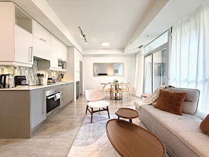 A modern kitchen with a dining area, a sofa, and a large window. - Cozy 2BR • Gym+Parking • Rogers Centre | MTCC (Toronto)