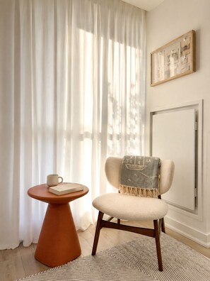A room with a chair, a small table, a book, a cup, and a painting on the wall. - Cozy 2BR • Gym+Parking • Rogers Centre | MTCC (Toronto)