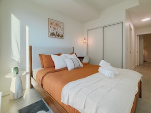 A hotel room with a bed, bedside table, lamp, and artwork. - Cozy 2BR • Gym+Parking • Rogers Centre | MTCC (Toronto)