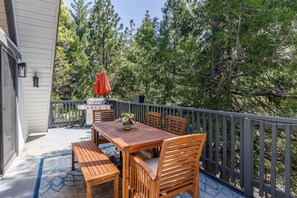 An outdoor patio with a wooden table and chairs, a grill, and a red umbrella. - Cozy 3-bedroom cabin in superb Lake Arrowhead (Lake Arrowhead)