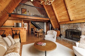 A spacious loft with a high ceiling, wooden beams, a stone fireplace, a dining area, and a cozy seating area with a fireplace. - Cozy 3-bedroom cabin in superb Lake Arrowhead (Lake Arrowhead)