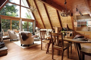 A spacious loft with a high ceiling, wooden beams, a dining area, and a large window offering a view of the outdoors. - Cozy 3-bedroom cabin in superb Lake Arrowhead (Lake Arrowhead)