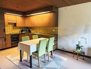 A modern kitchen with wooden cabinets, a built-in oven, and a dining area with a table and chairs. - Mountain View Lodge by Interhome (Sörenberg)