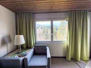 A room with a single window, a chair, a table with a lamp, and a remote control. - Mountain View Lodge by Interhome (Sörenberg)