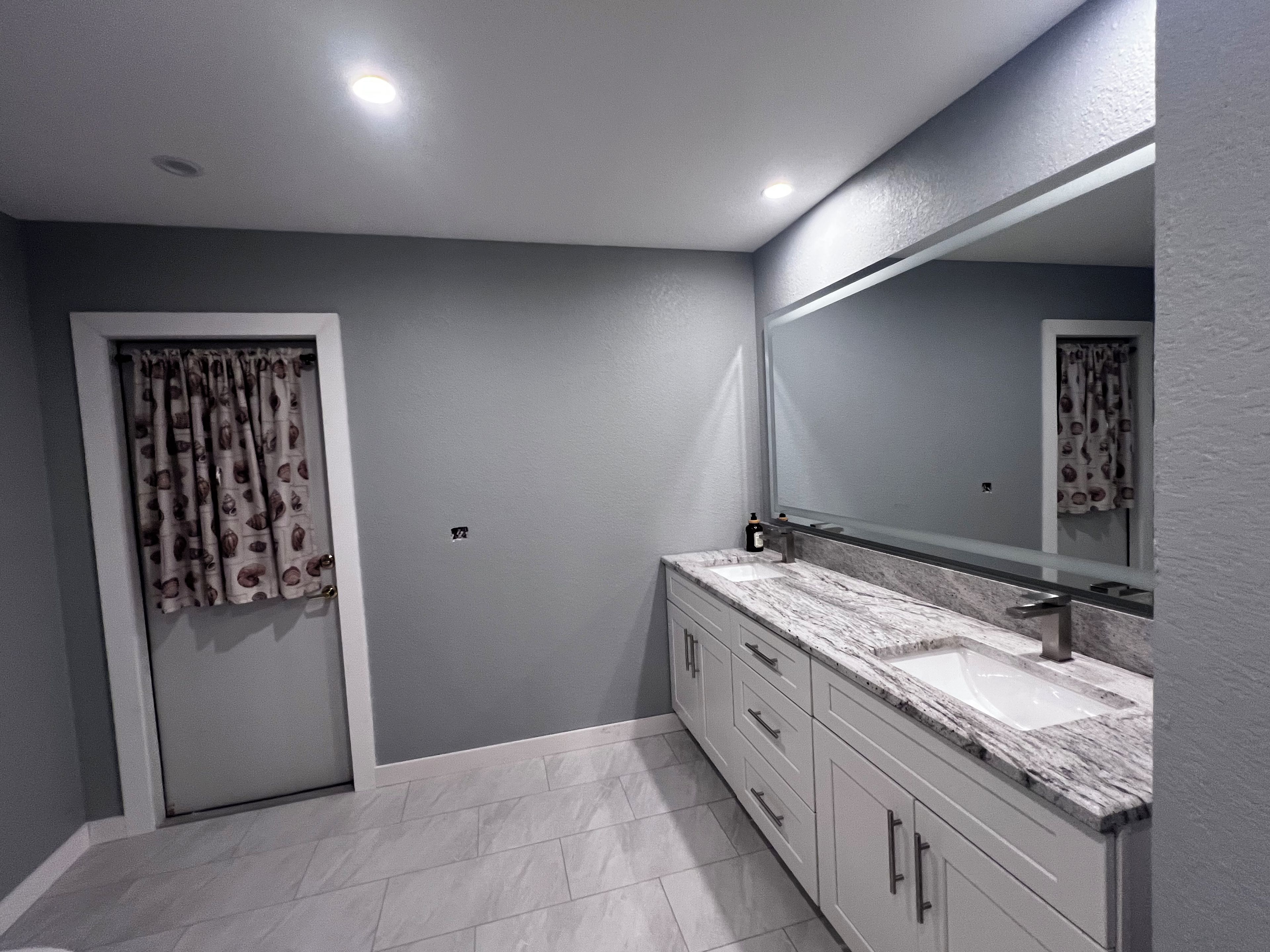 A bathroom with a white vanity, a large mirror, and a shower area.